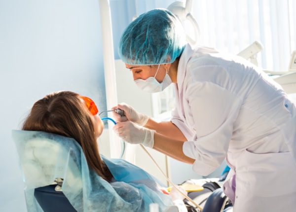 A female dentist prepares to operate on her patient who wears orange glasses